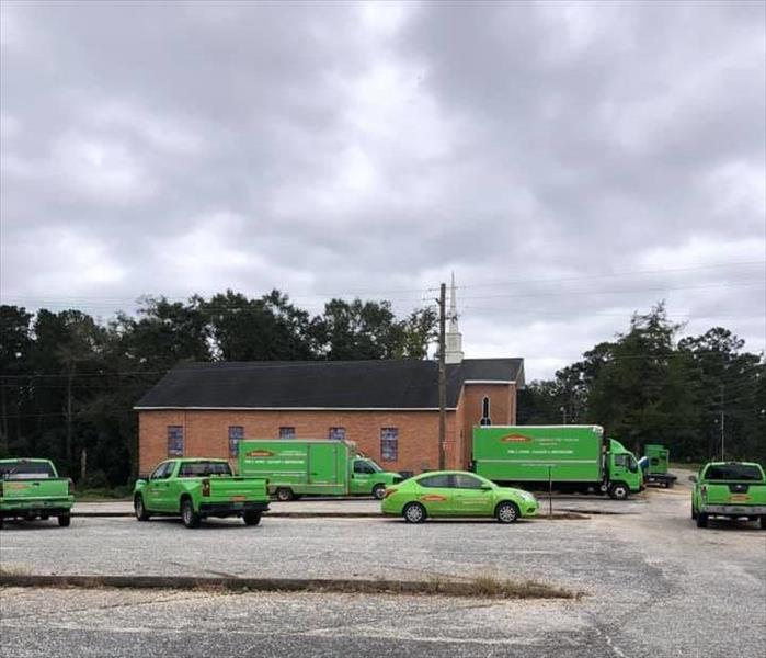 Multiple green vehicles parked on a gray parking lot outside a red brick church.